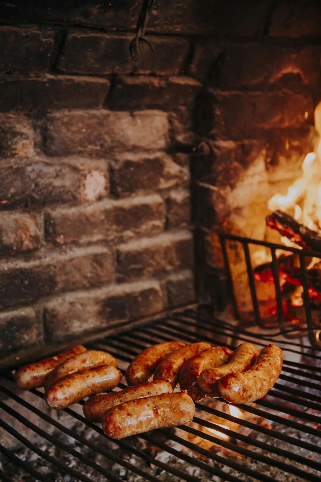 Chorizos dorándose en la parrilla, con el fuego de leña al fondo